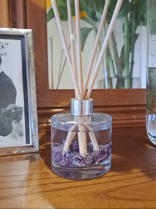 Reed diffuser with amethyst crystals placed on a table next to flowers and mirror
