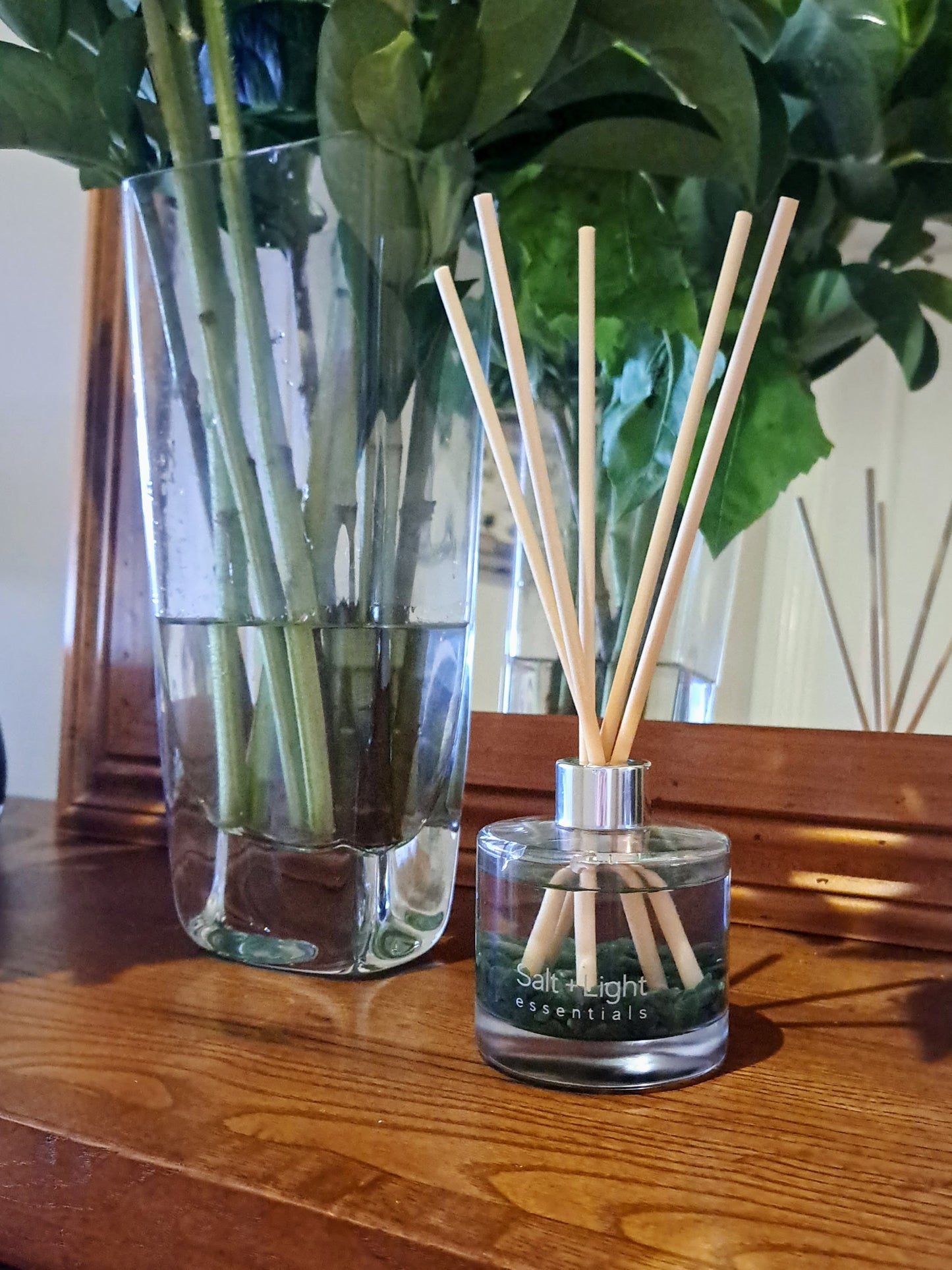 Reed diffuser with green aventurine crystals positioned on a table next to vase with flowers and mirror