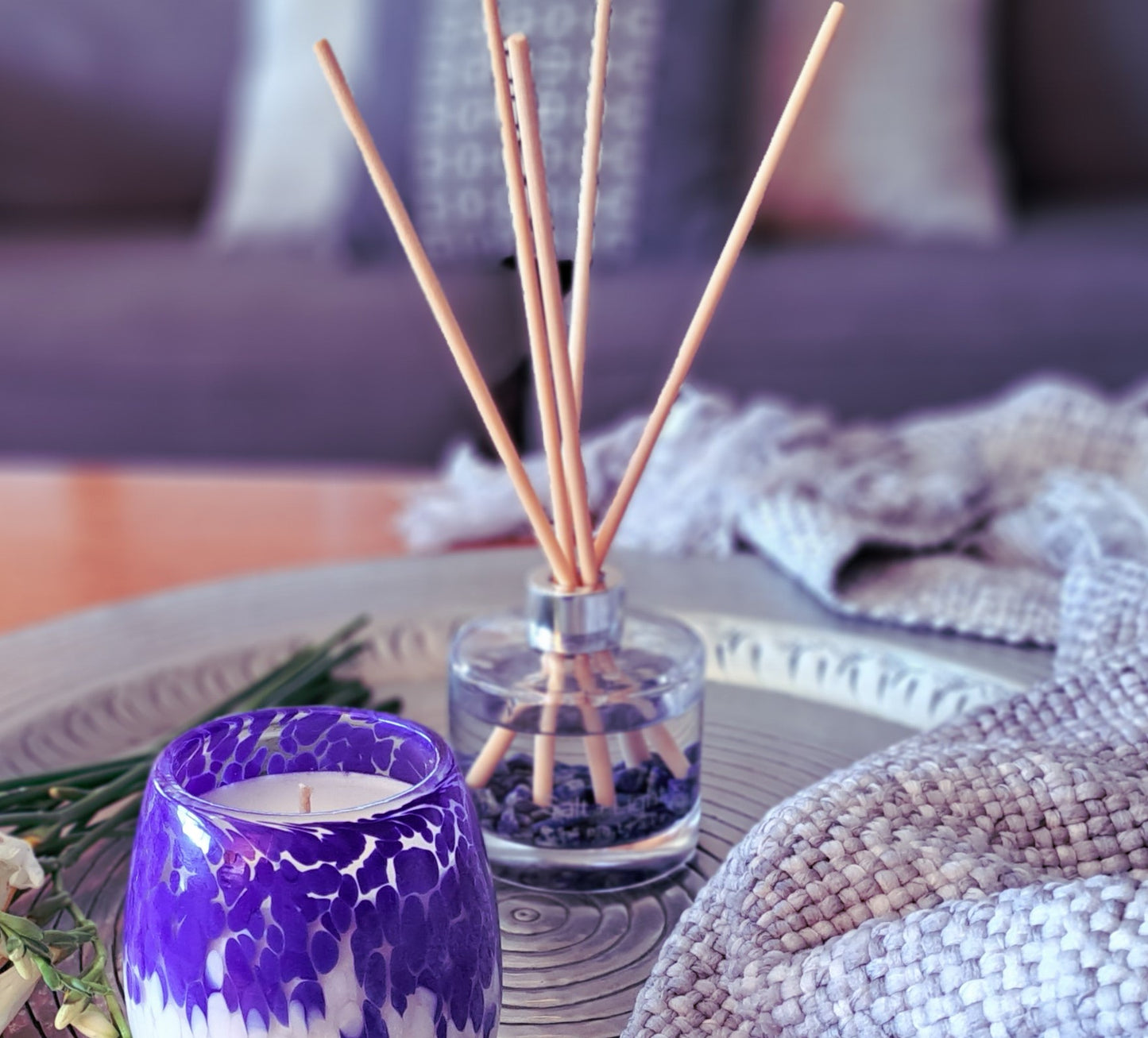 Reed diffuser with lapis lazuli crystals positioned on a silver tray next to  a candle and flowers