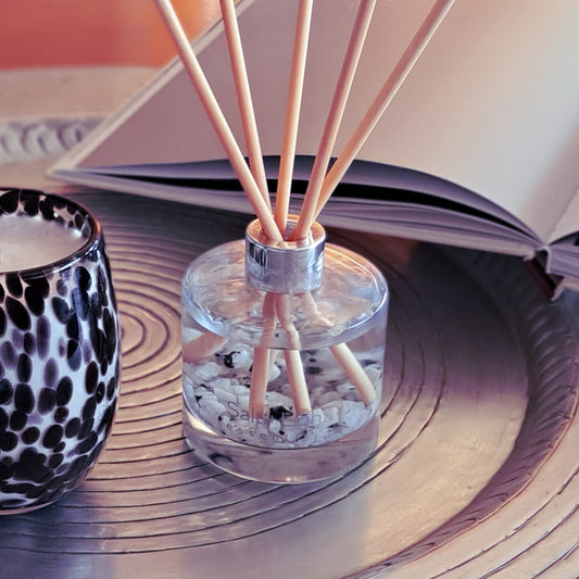 Reed diffuser with moonstone crystals on a silver tray next to a candle and a book