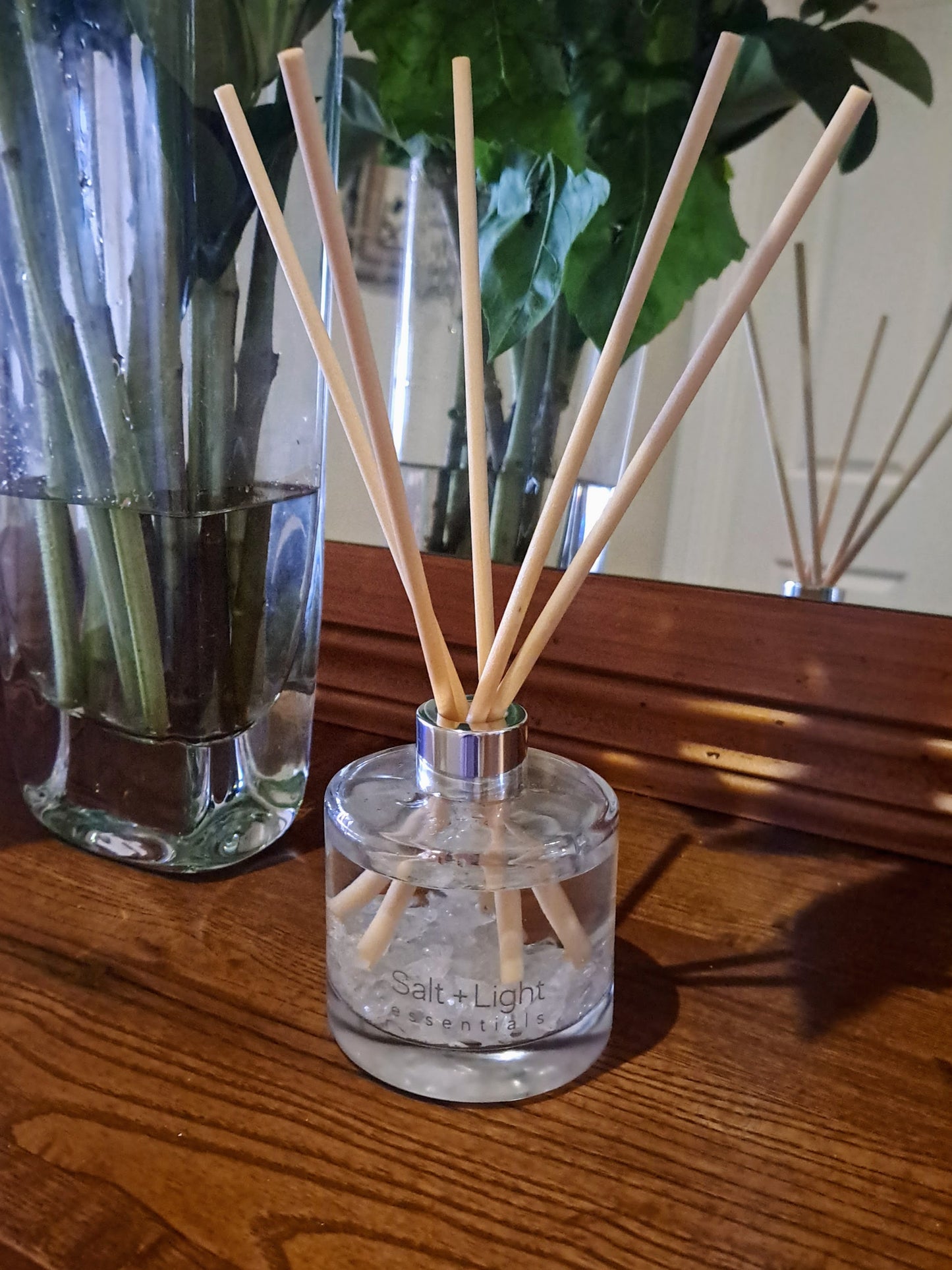 Reed diffuser with clear quartz crystals positioned on a table next to vase with flowers and mirror