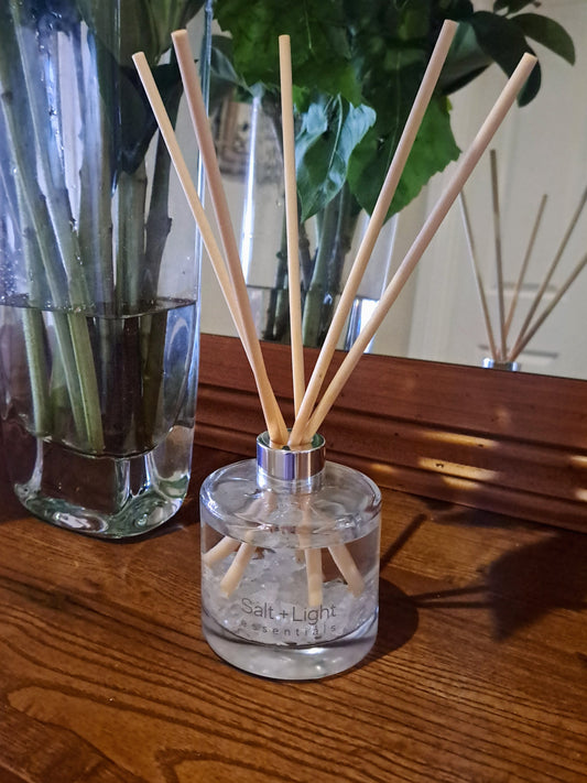 Reed diffuser with clear quartz crystals positioned on a table next to vase with flowers and mirror