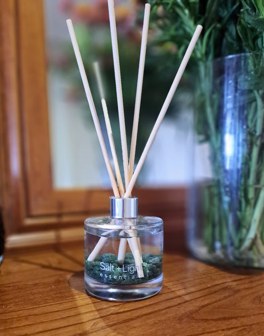 Reed diffuser with green aventurine crystals positioned on a table next to vase with flowers and mirror