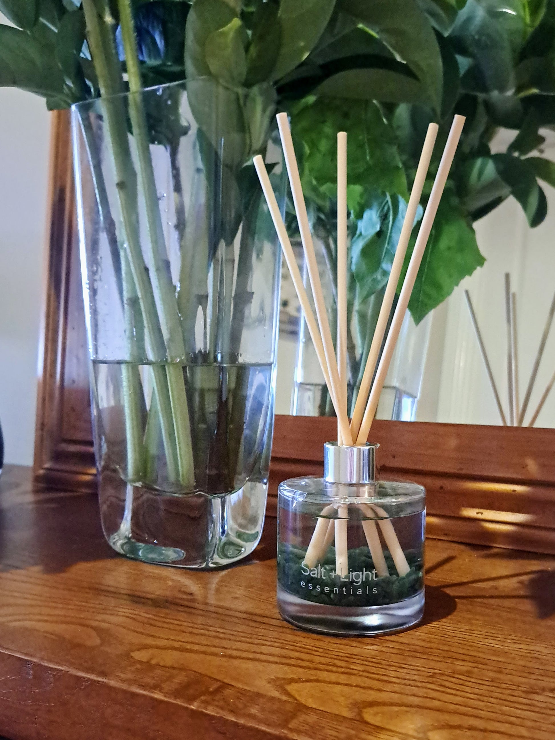 Reed diffuser with green aventurine crystals positioned on a table next to vase with flowers and mirror