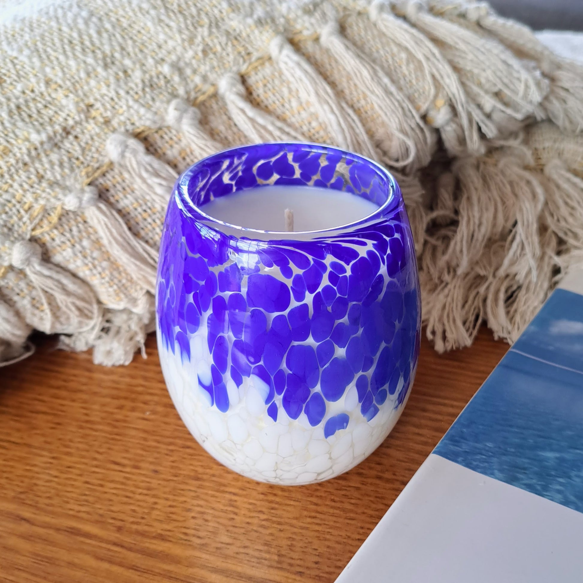 Blue and white candle vessel on a table next to a blanket