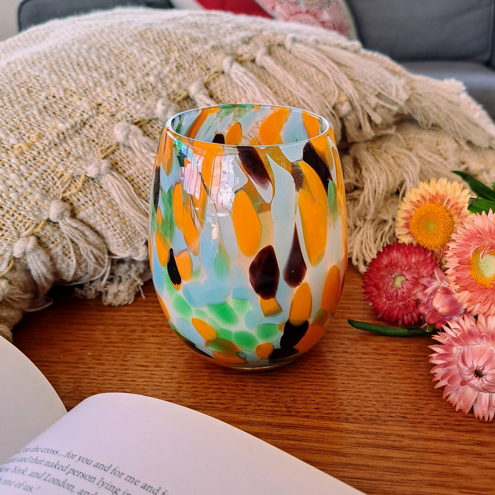Orange and green candle vessel on a table next to flowers and a book