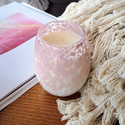 Pink and white candle on a table next to a blanket and a book