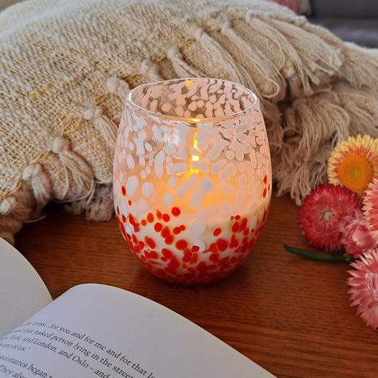 Lit red and white candle vessel on a table next to flowers and a book