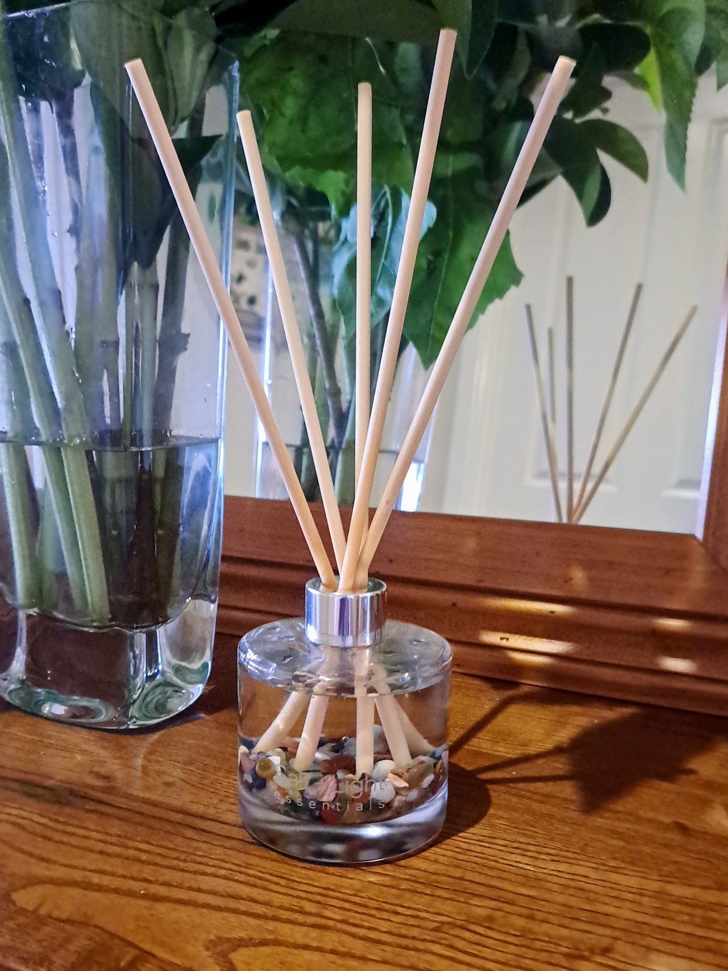 Reed diffuser with mixed crystal chips on a table next to flowers and a mirror
